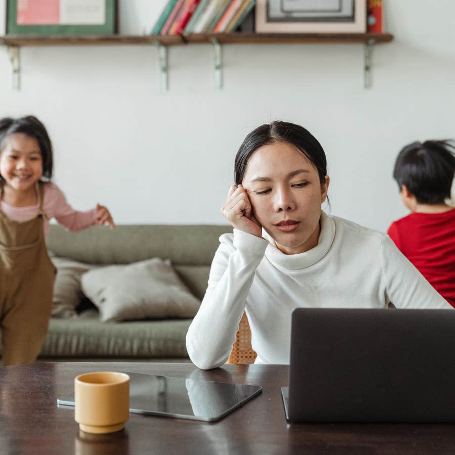 woman using her laptop while kids play in the background