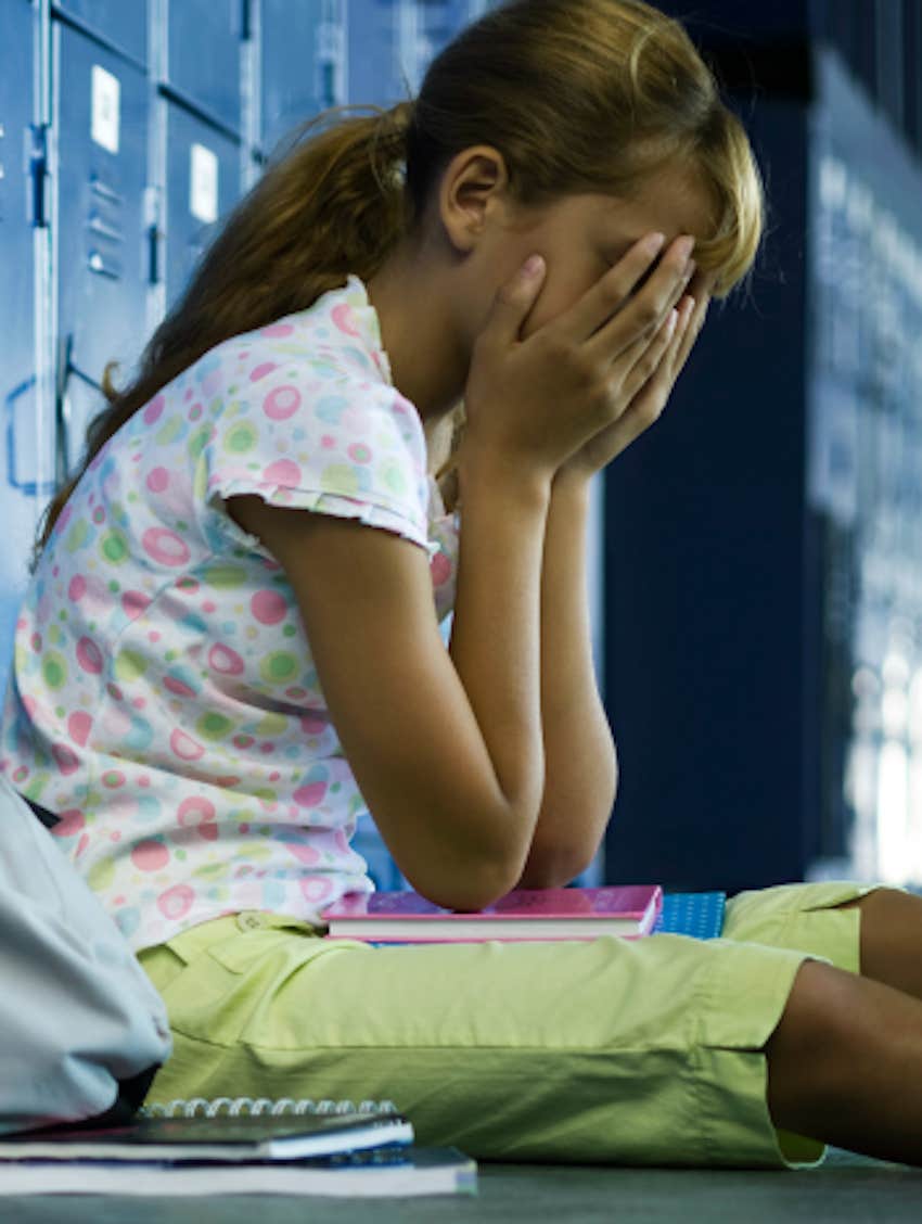 student sits on hall floor with face in hands