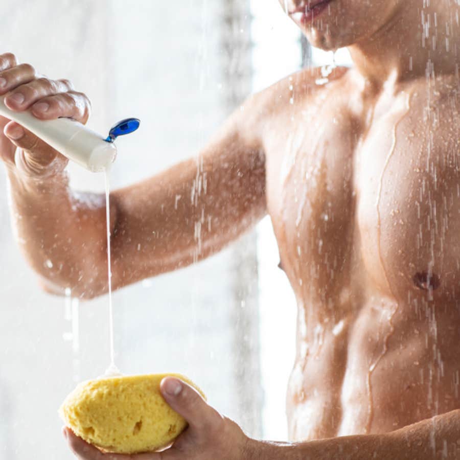 man putting body wash on a loofah in the shower