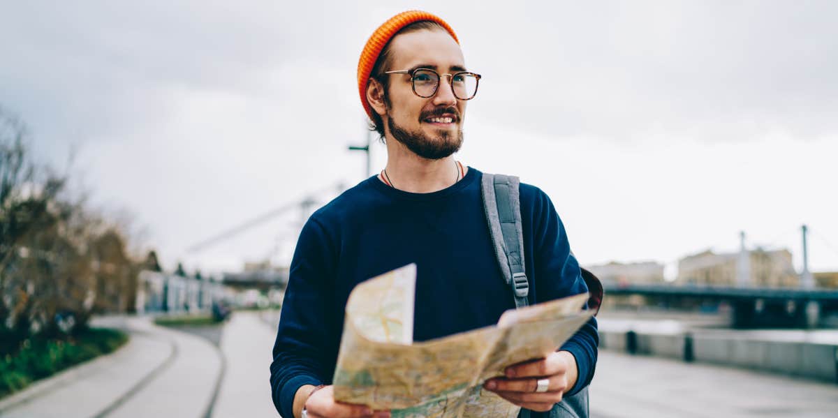 smiling male traveler walking with map having city tour excited with urban setting on autumn weekends