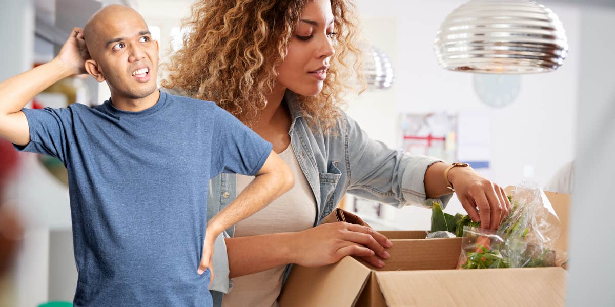 Woman putting groceries away, man confused at what he forgot