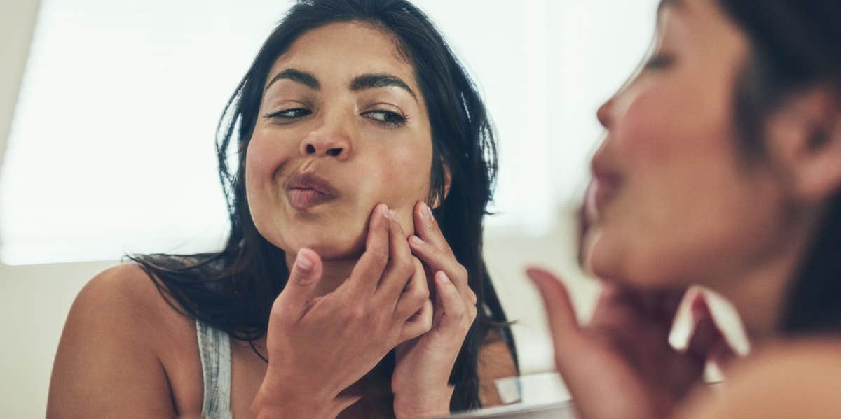 woman popping pimple in mirror