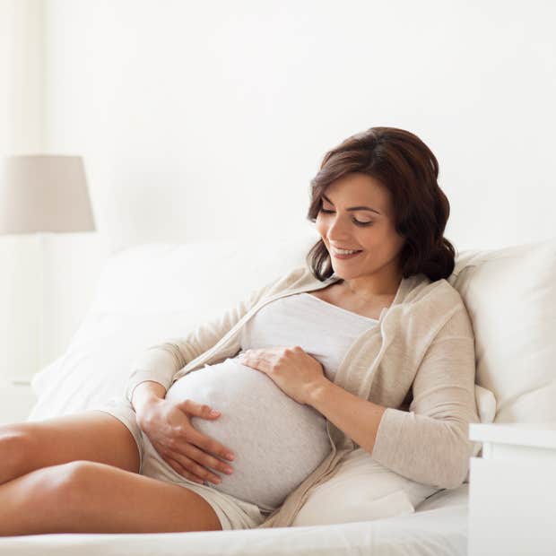 Pregnant woman in bed holding her stomach and smiling.