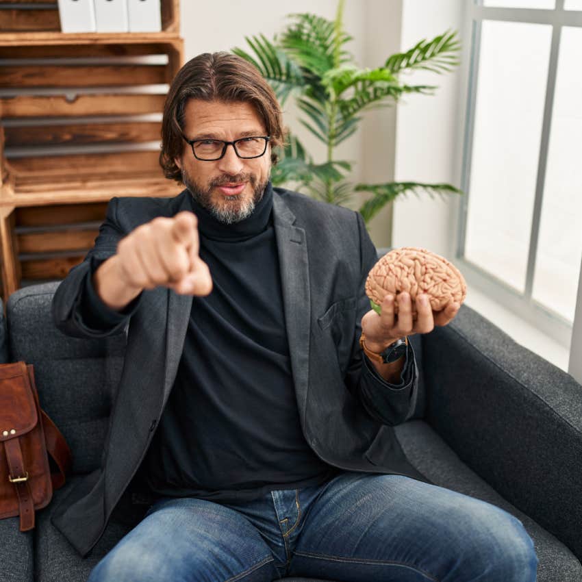 Handsome middle age man at consultation office holding brain pointing with finger to the camera
