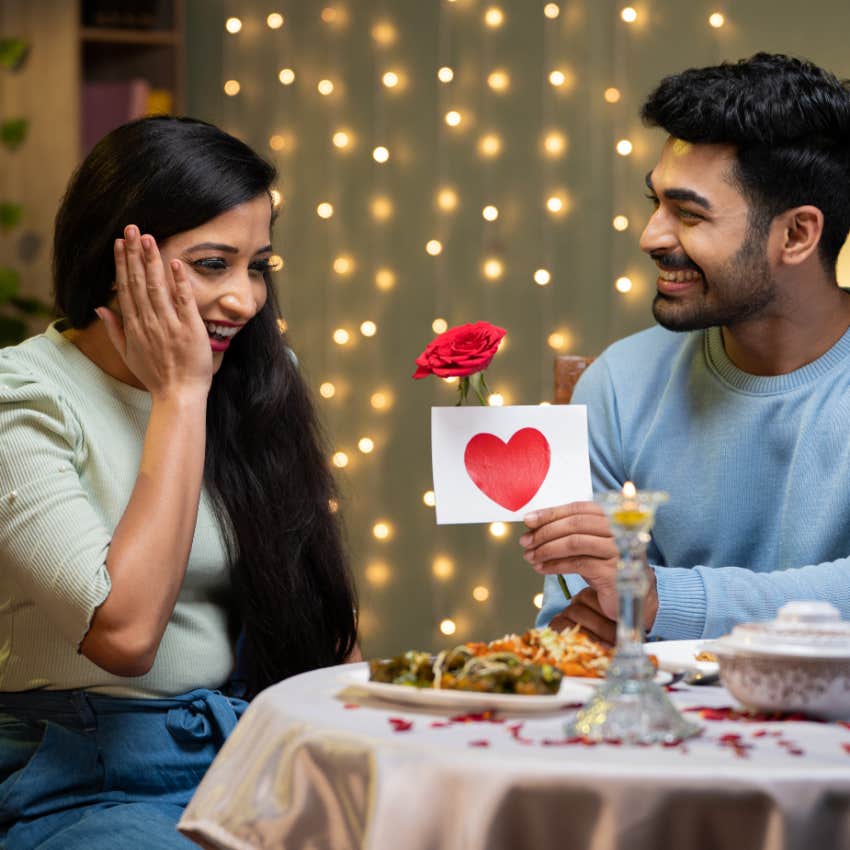 Happy young man proposing to excited girl with rose during candle light dinner