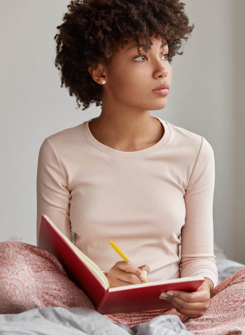 woman thinking deeply while writing in journal