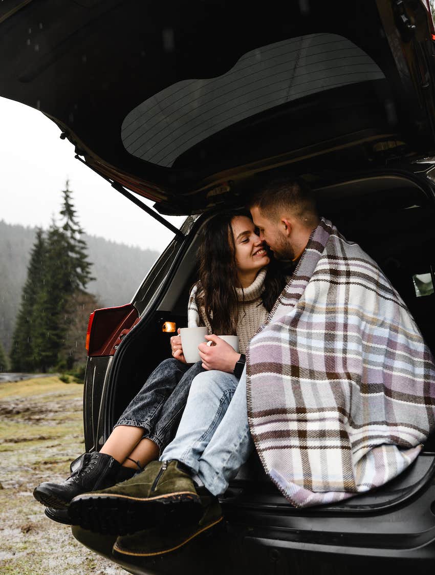 couple cuddle in hatchback of car while camping