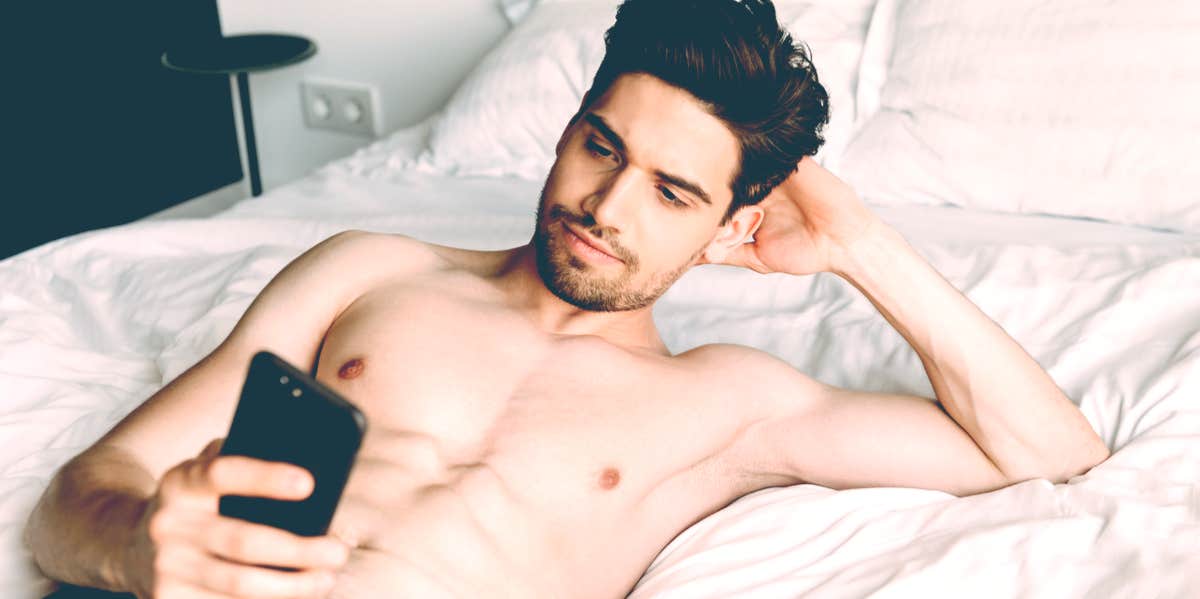 shirtless man texting in bed