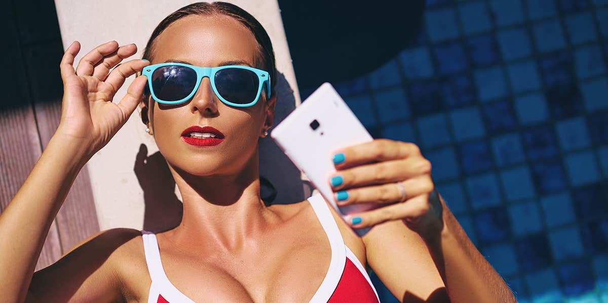 woman laying by pool in bikini taking selfie