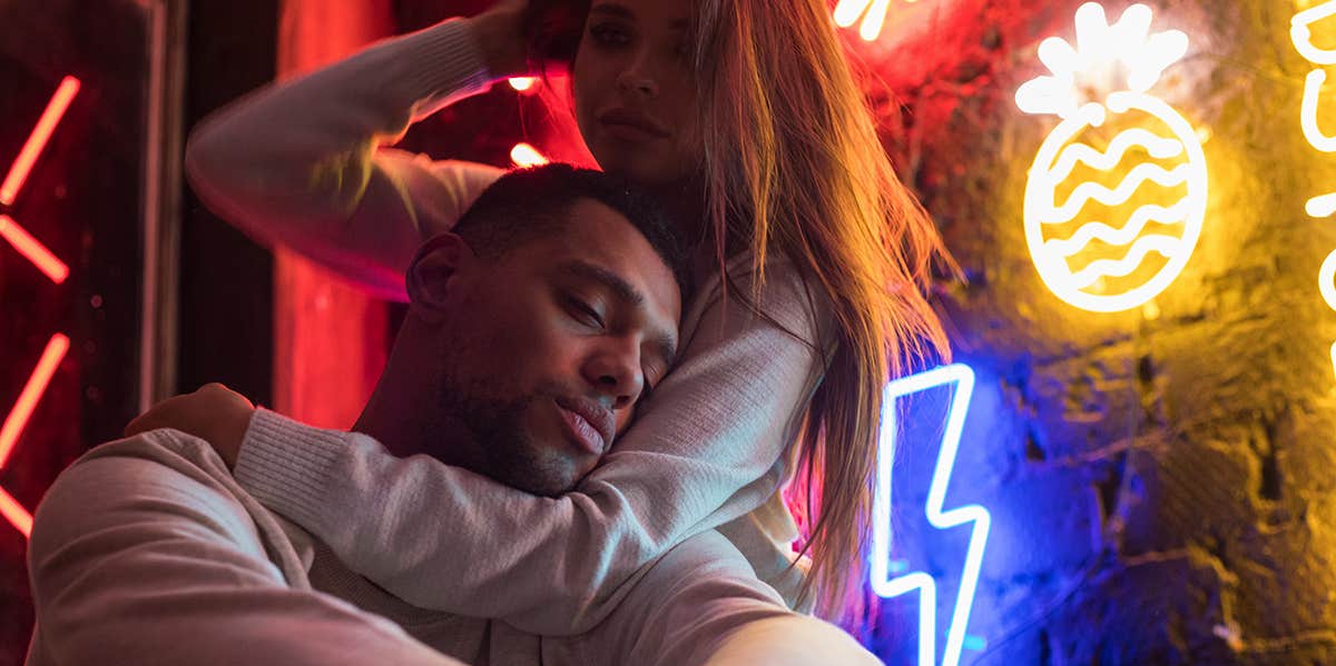Harsh Signs You're Dating A Spoiled Brat woman cuddling man near neon sign