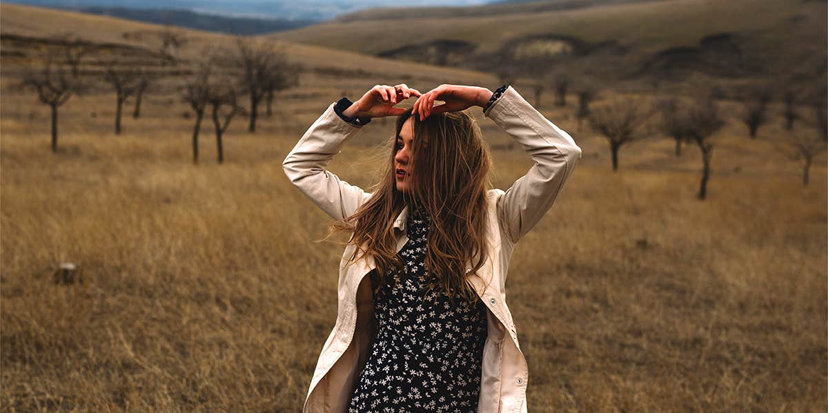 young woman in dress and jacket standing in open field