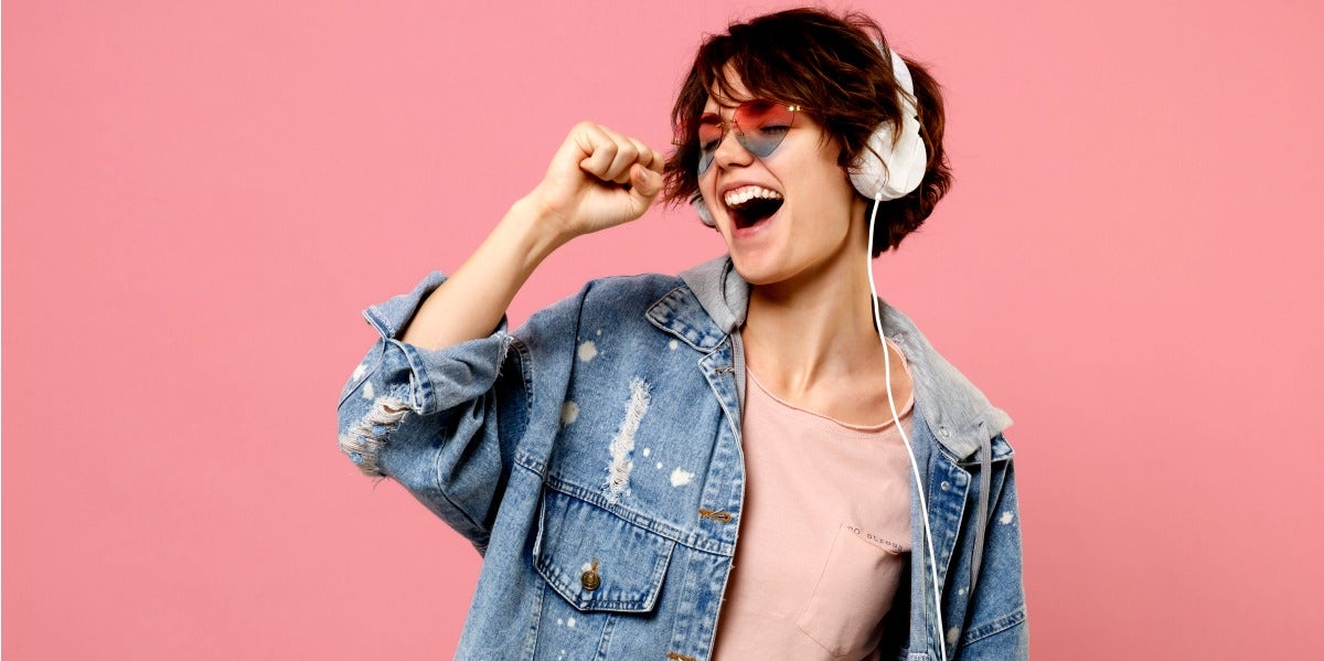 woman listening to music on headphones with pink background