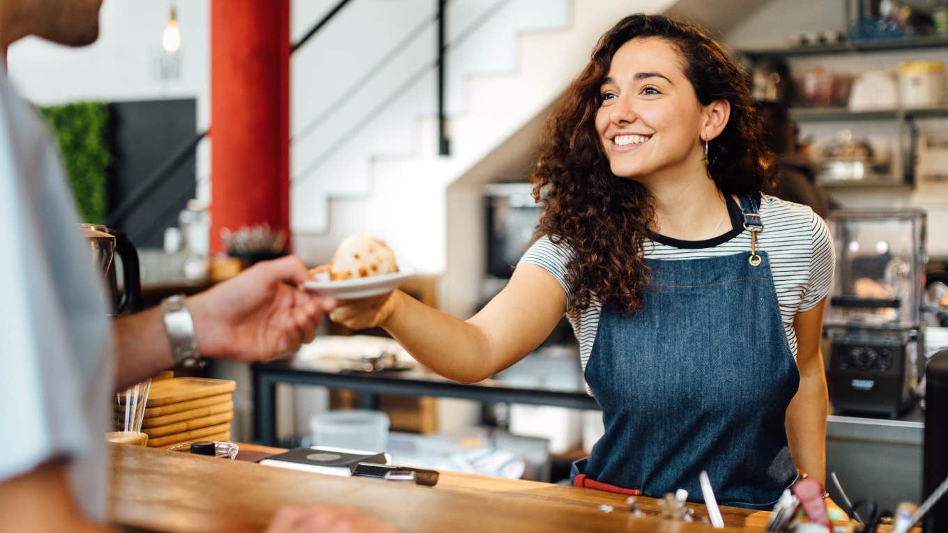 Corporate Woman Reveals Why She Got A Job As A Coffee Barista Barista handing a customer a pastry.