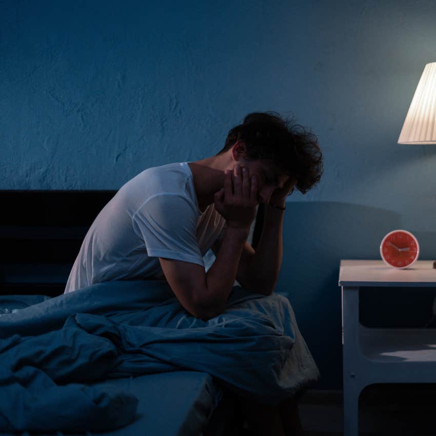 exhausted man sitting on edge of bed in dimly lit bedroom