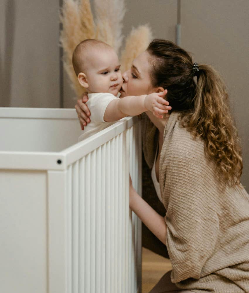 mom kissing baby in his crib