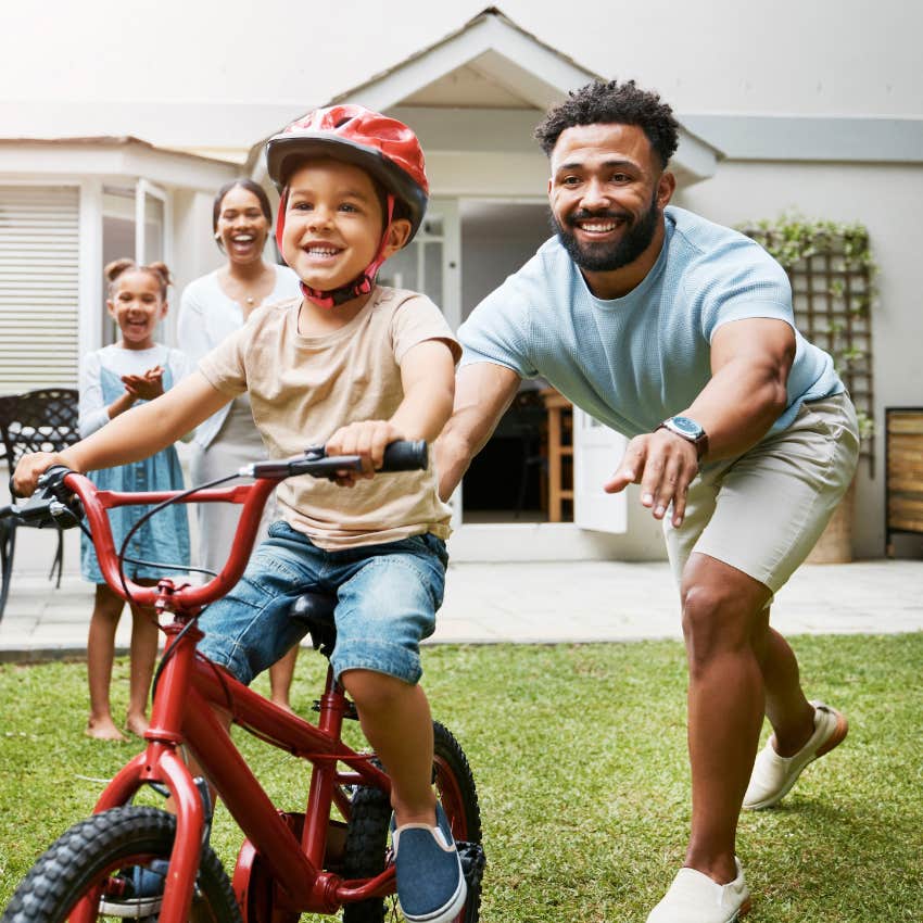 little boy riding a bike with his dad's help