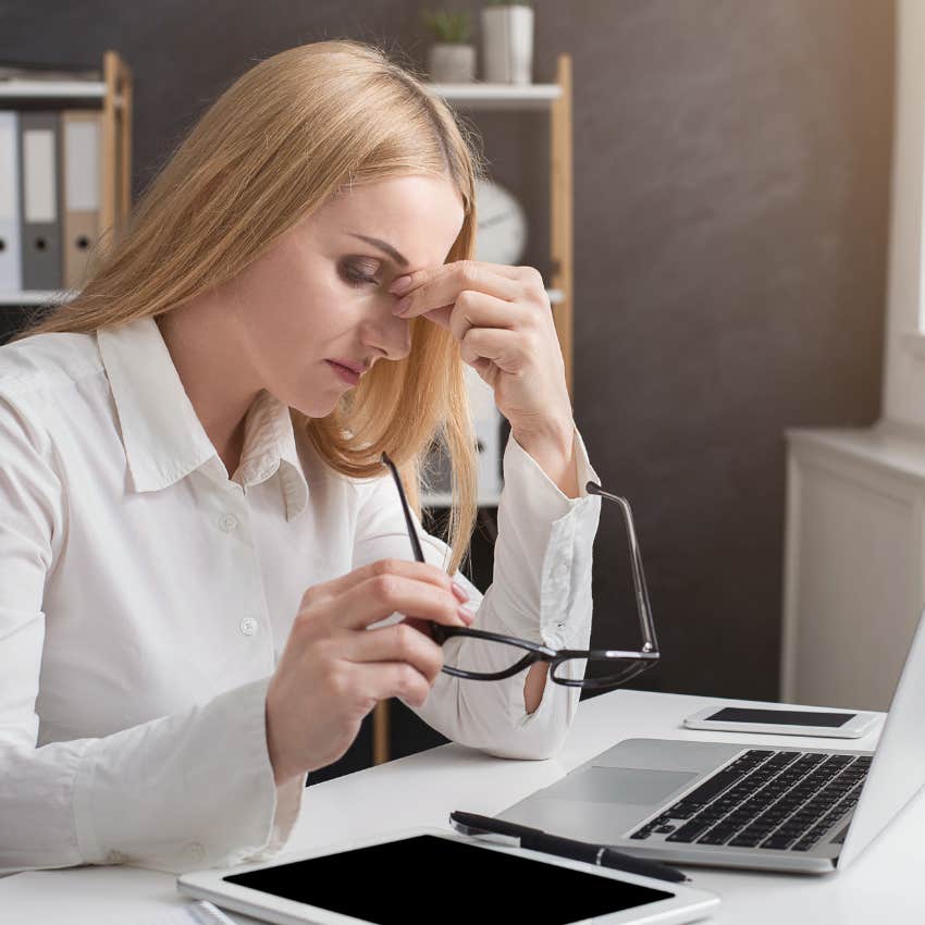 blonde woman sitting at work desk pinching the bridge of her nose