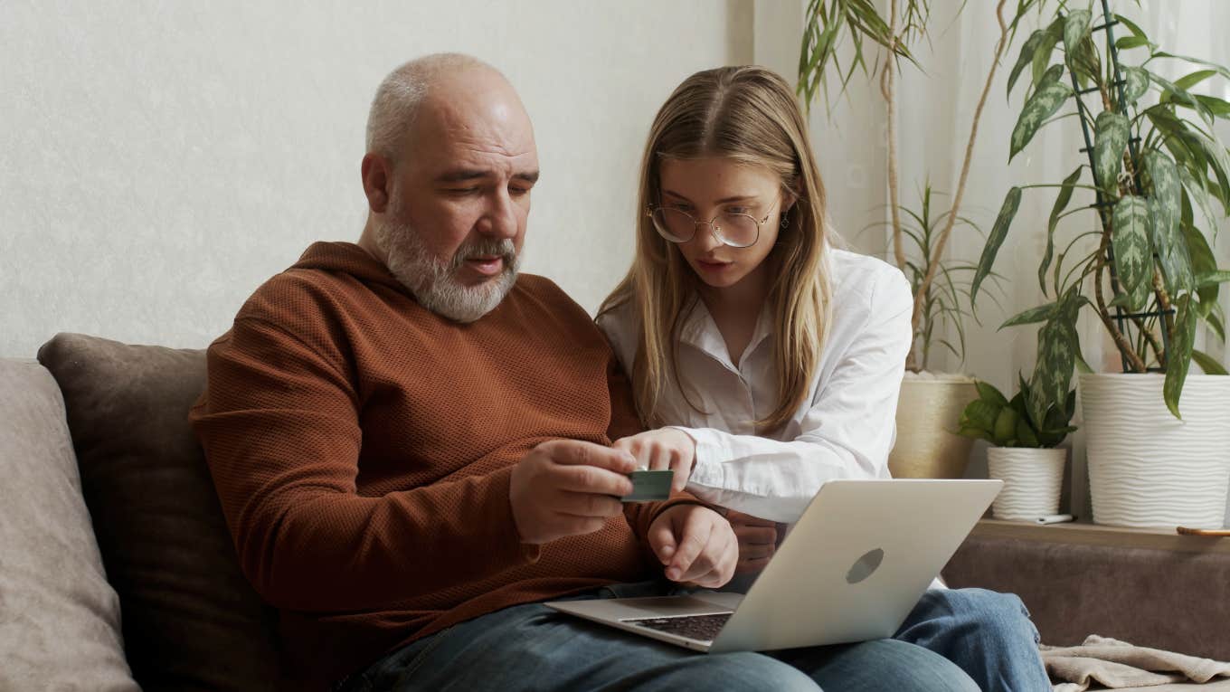 young woman showing her older father how to use a bank card and computer at home