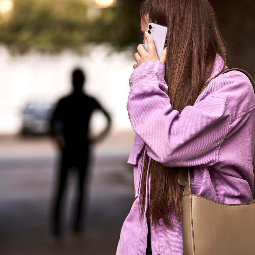 woman talking on phone and looking back at silhouette of man following her