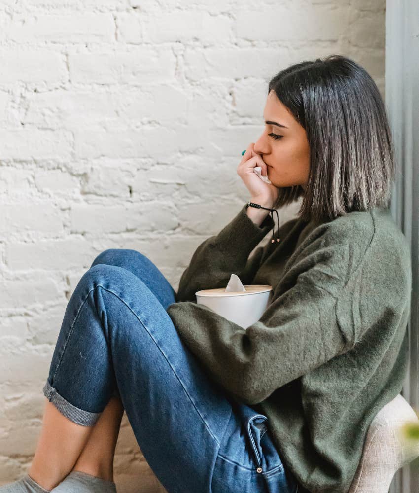 woman sitting on a couch knees to chest holding a box of tissues