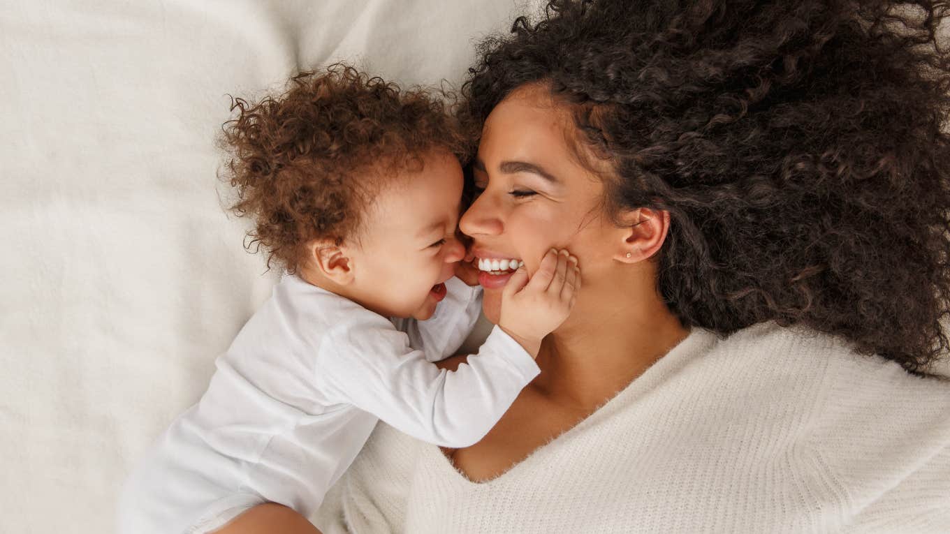 mother smiling while cuddling with baby on bed