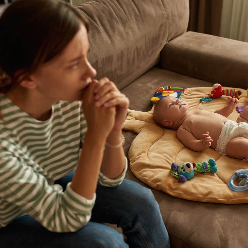 baby lying on flat pillow placed on sofa, young exhausted mother sitting near, looking away