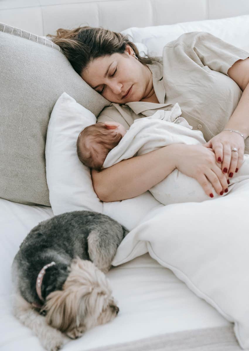 mom holding baby with dog in bed