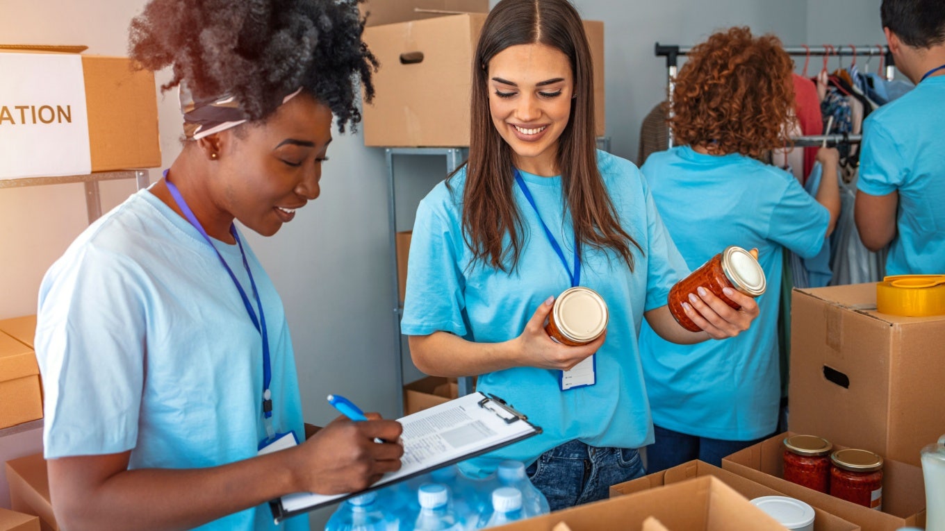 Group of people working in charitable foundation. Happy volunteer looking at donation box on a sunny day. Happy volunteer separating donations stuffs. Volunteers sort donations during food drive Food bank workers sorting food