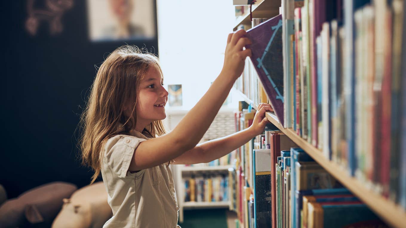 little girl pulling a book off of a shelf