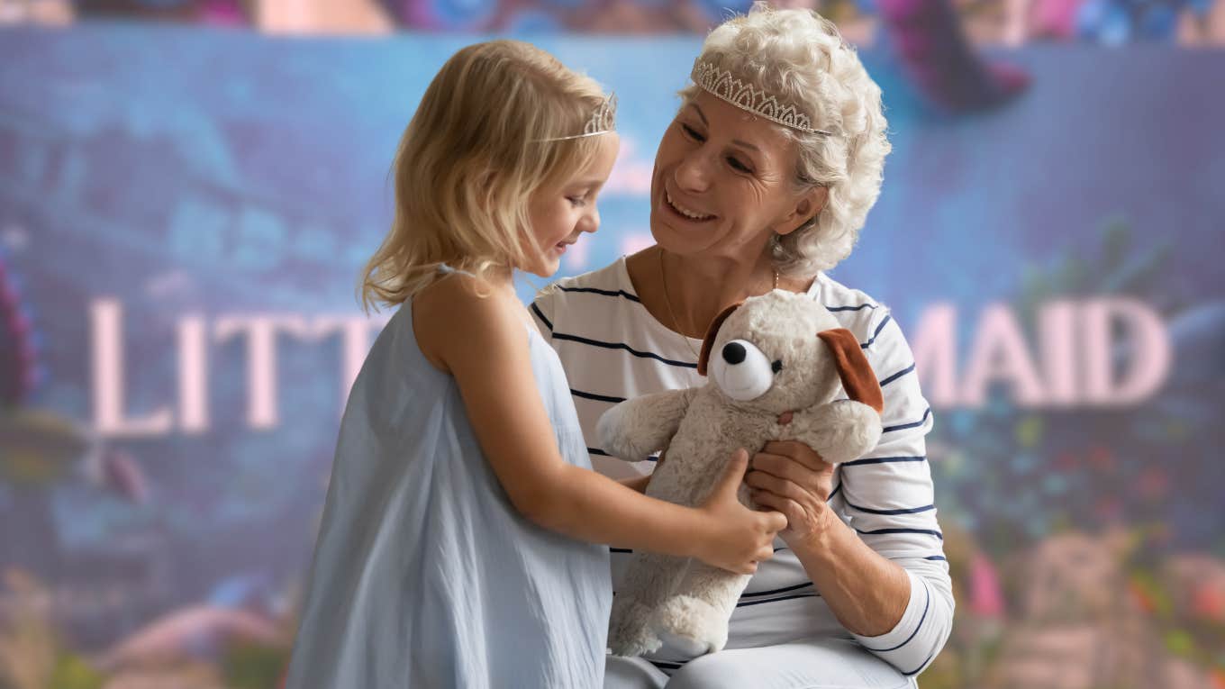 Grandma talking to little girl in front of The Little Mermaid backdrop. 