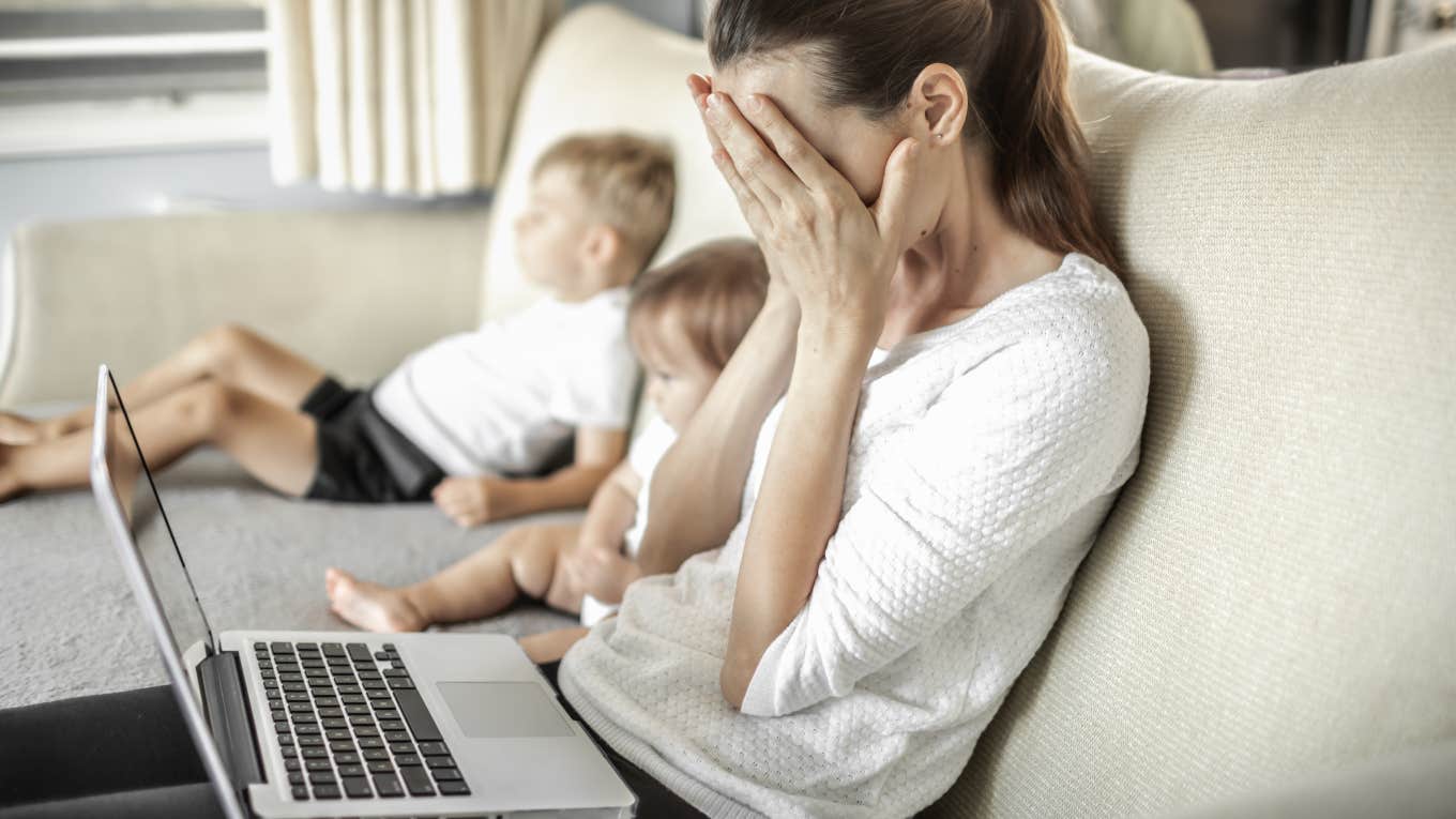Husband Refuses To Give His Stay-At-Home Wife Access To Money sad, stressed mom on laptop sitting on couch next to kids