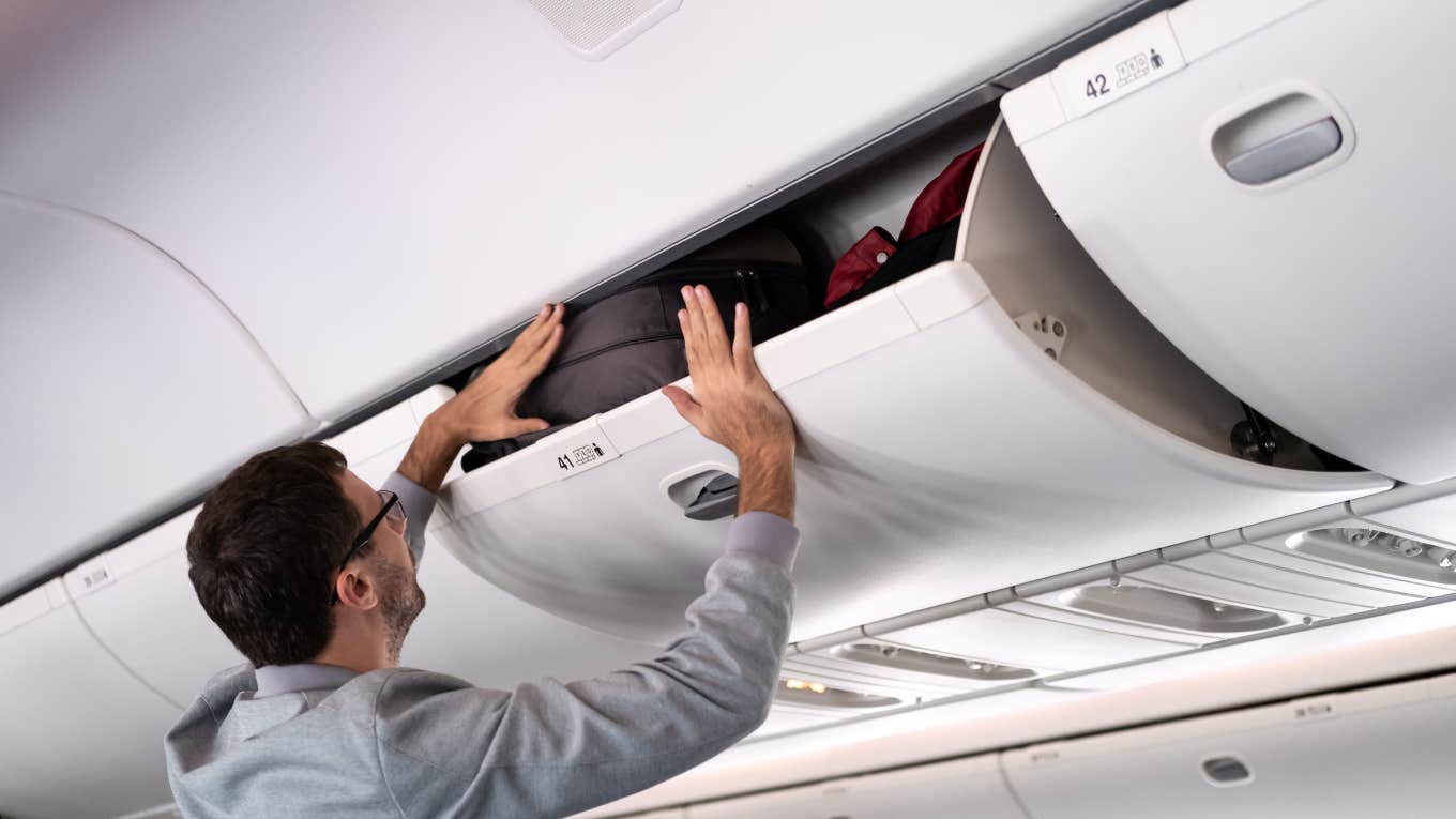 man putting suitcase in airplane overhead bin