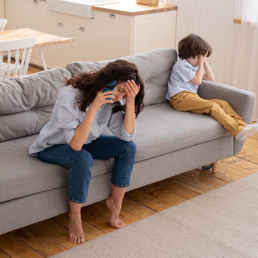 tired mom on the phone while sitting on the couch next to upset toddler