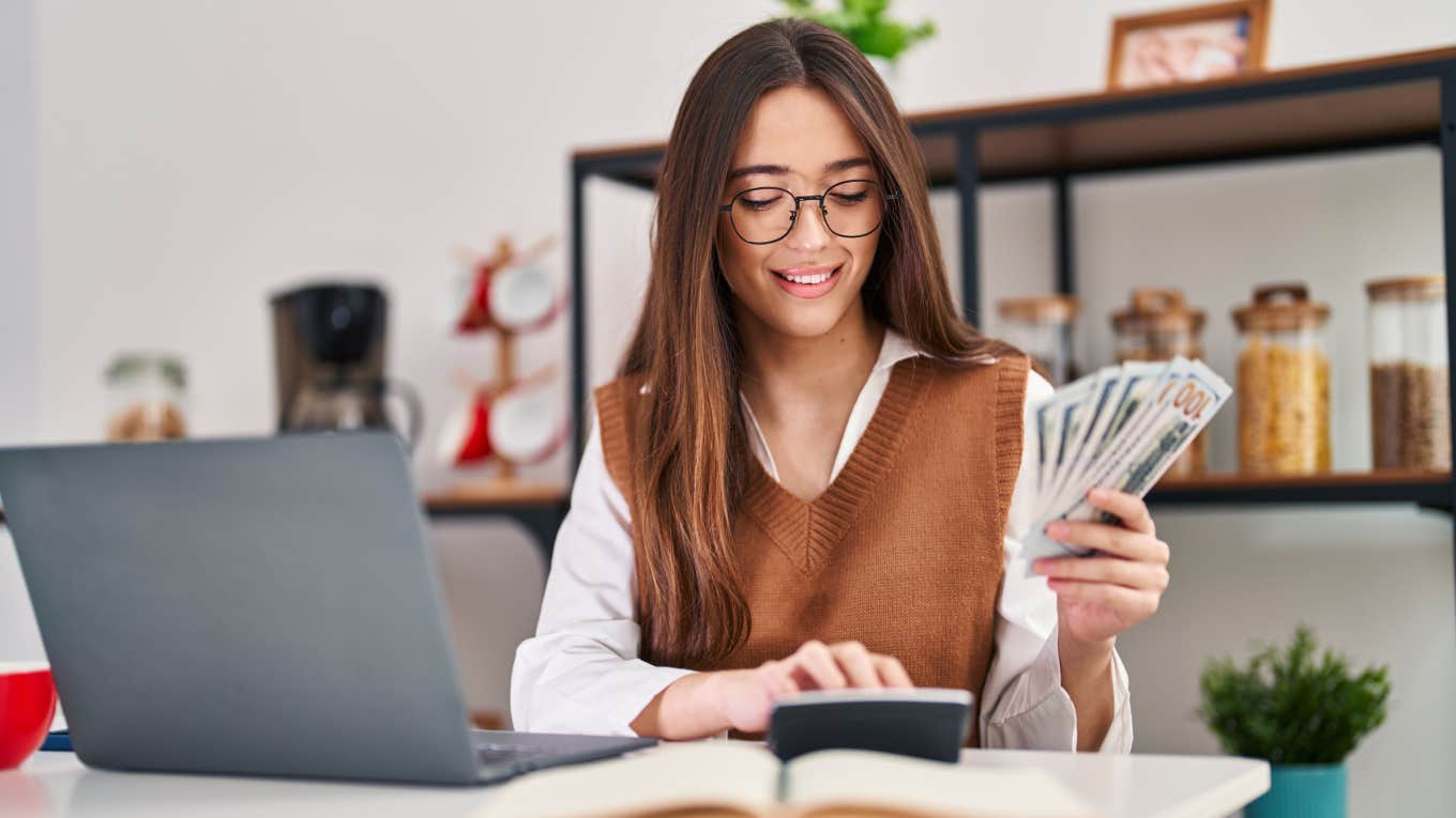 Neurodivergent Woman Shares 3 Ways She Tricked Herself Into Saving Over $1314 woman counts her saved up cash at home in front of laptop