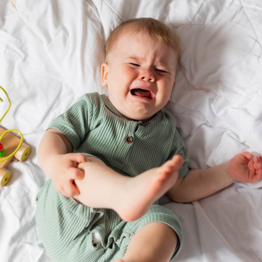 baby in a green cotton bodysuit is crying lying in bed with wooden educational toys