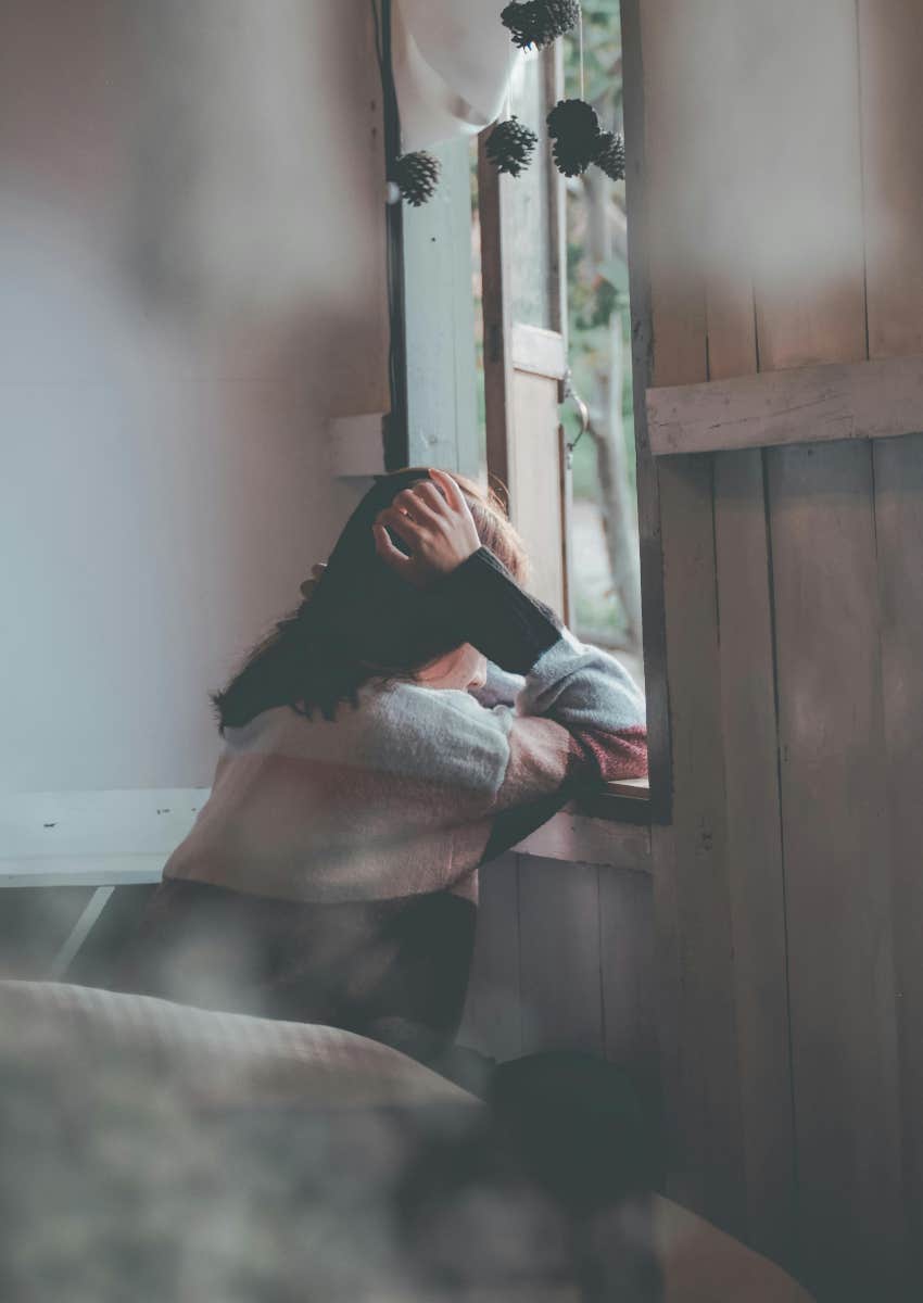 sad woman sitting at window looking out