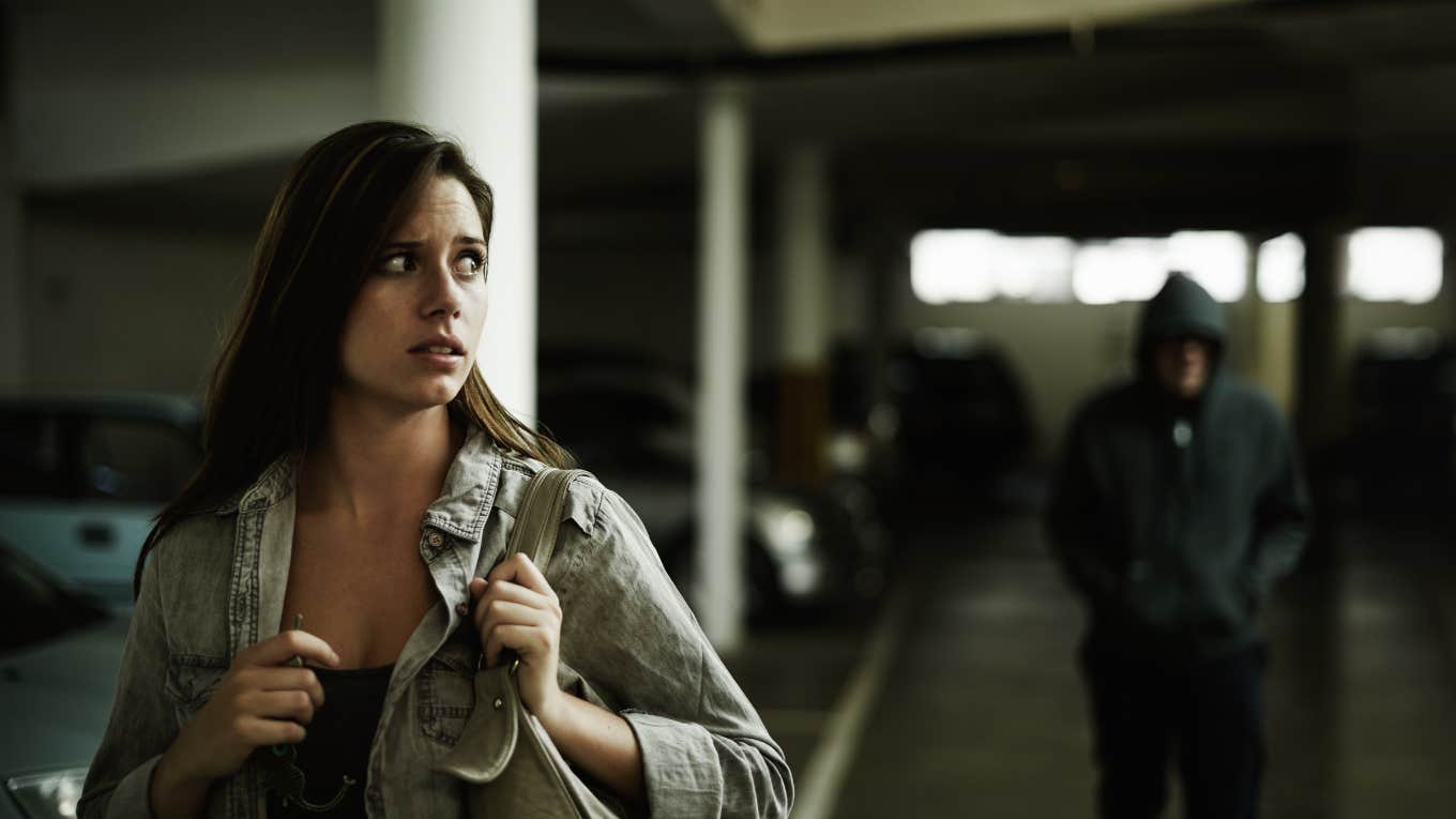 oung woman in a parking lot looking concerned as someone follows her.