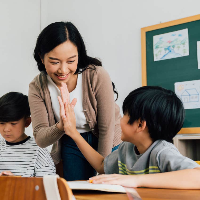 Teacher smiling while high-fiving a student. 