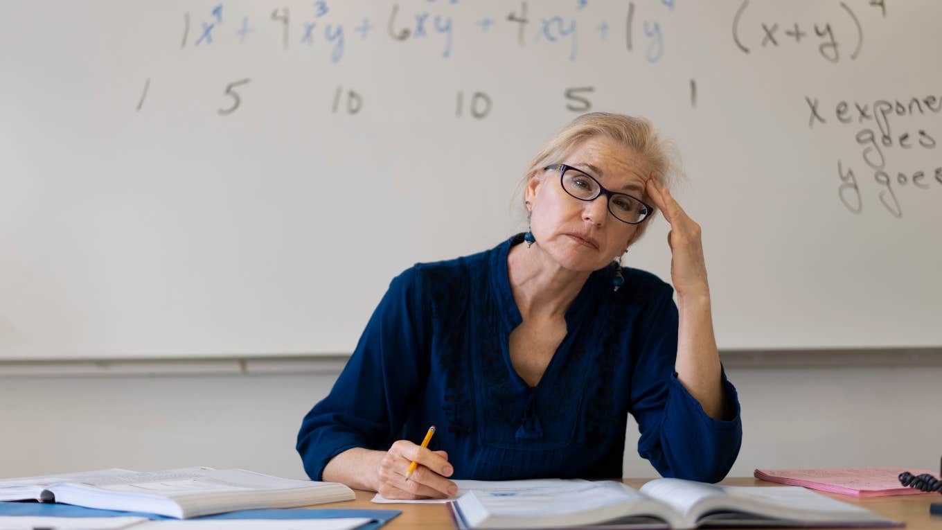 Teacher Says They're Pressured To Promote Students That Didn't Deserve It frustrated teacher sitting at desk in front of white board
