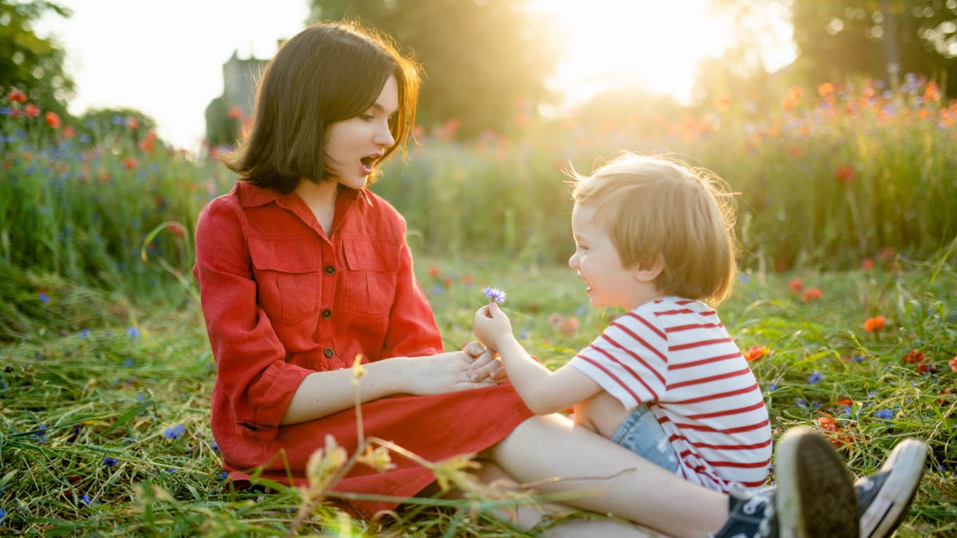 Teen With Temporary Custody Of Her 'Feminine' Brother Asks How To Balance His Feelings With Their Dad's Expectations teen sits in flower field with toddler brother