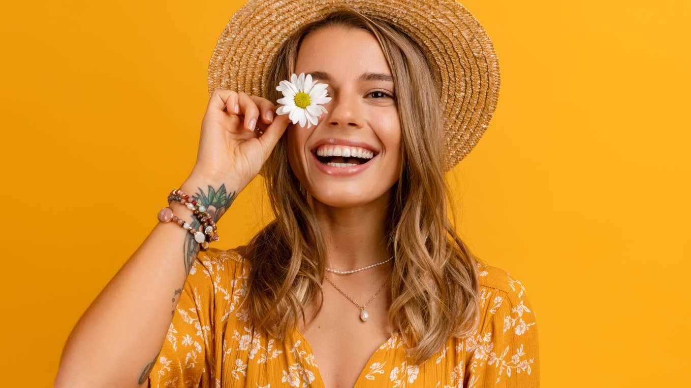happy woman holding daisy in front of yellow background