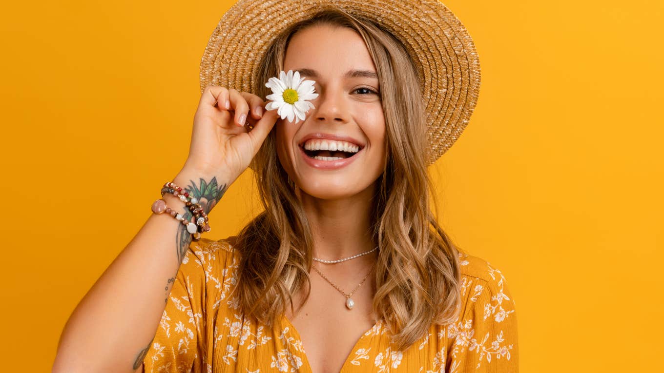The One Thing You Need To Accept If You Want To Grow happy woman holding daisy in front of yellow background