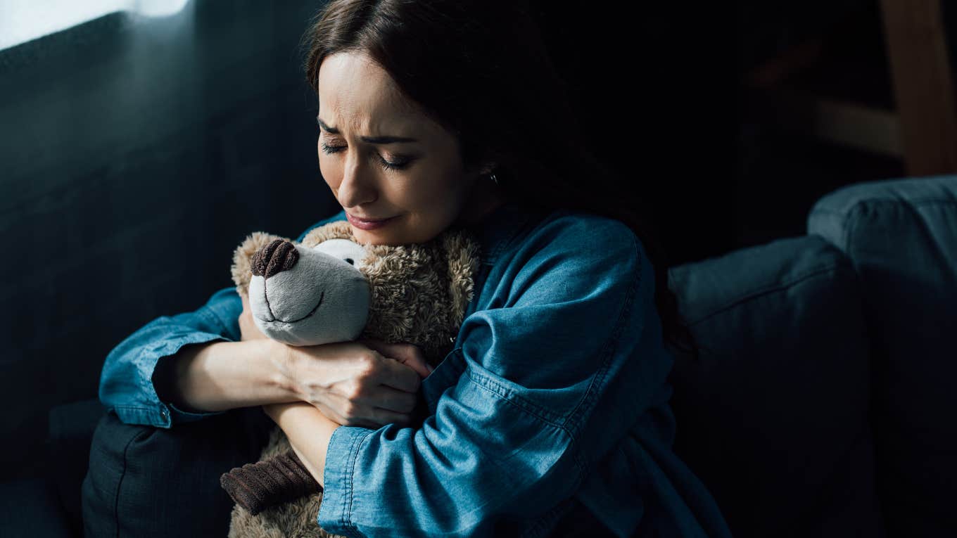Woman Breaks Up With Boyfriend And Destroys His Legos After He Throws Away Her Special Teddy Bear sad brunette woman with closed eyes holding teddy bear in living room