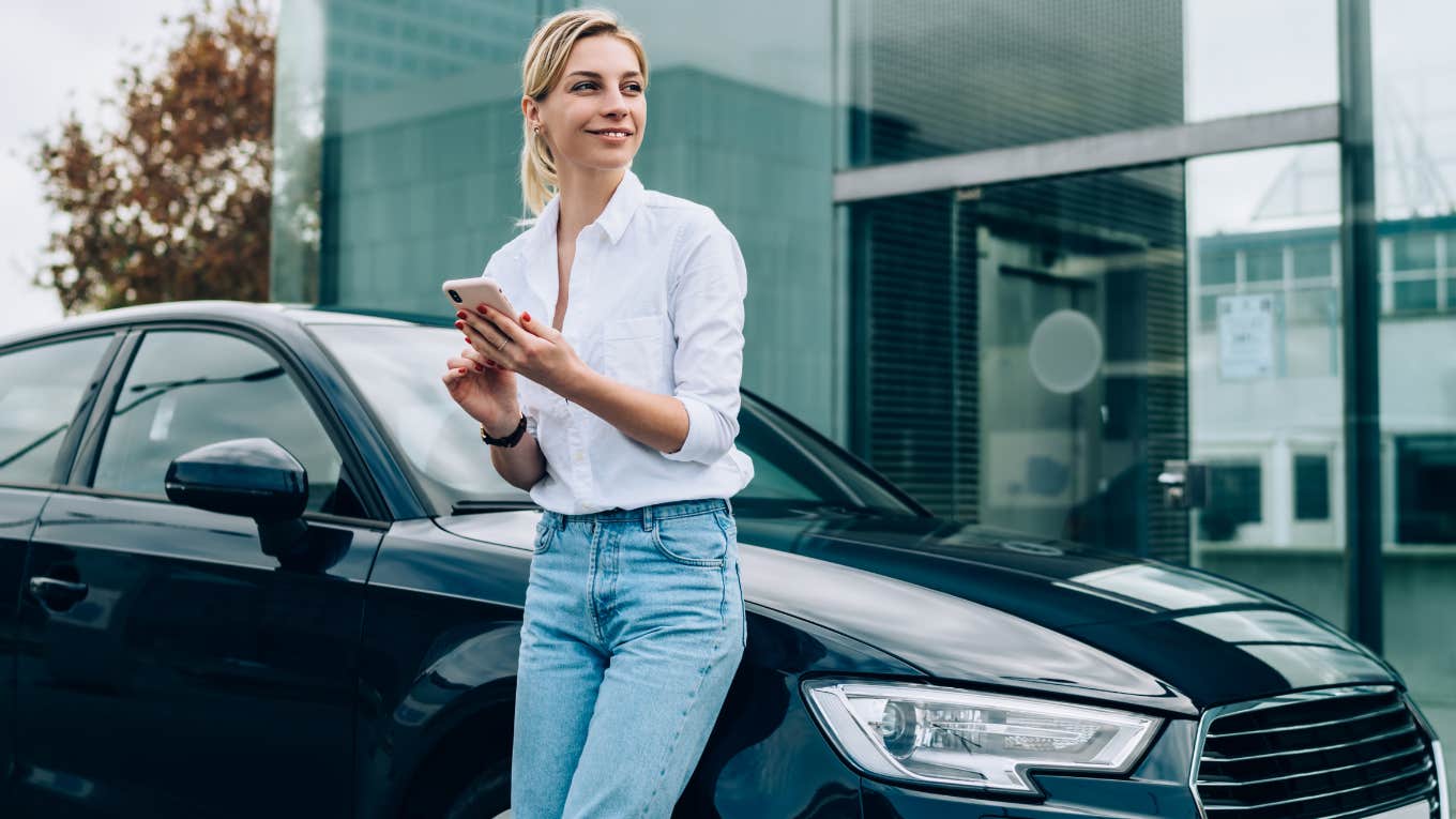 Woman Defends Decision To Purchase $100K Car Instead Of Buying A Home Woman leaning up against black car.