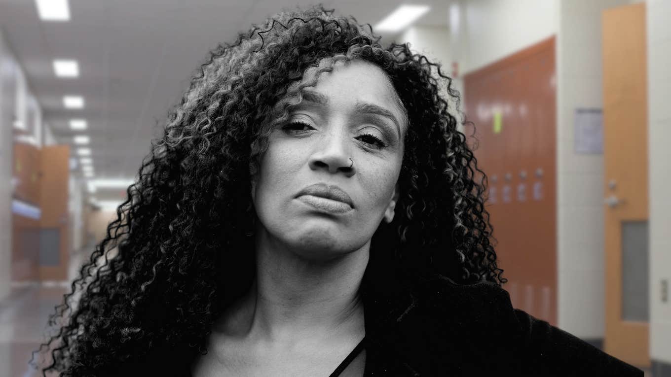 Woman Recalls Harmful 'Ranking List' In High School By Male Classmates Woman looking upset in a high school hallway.