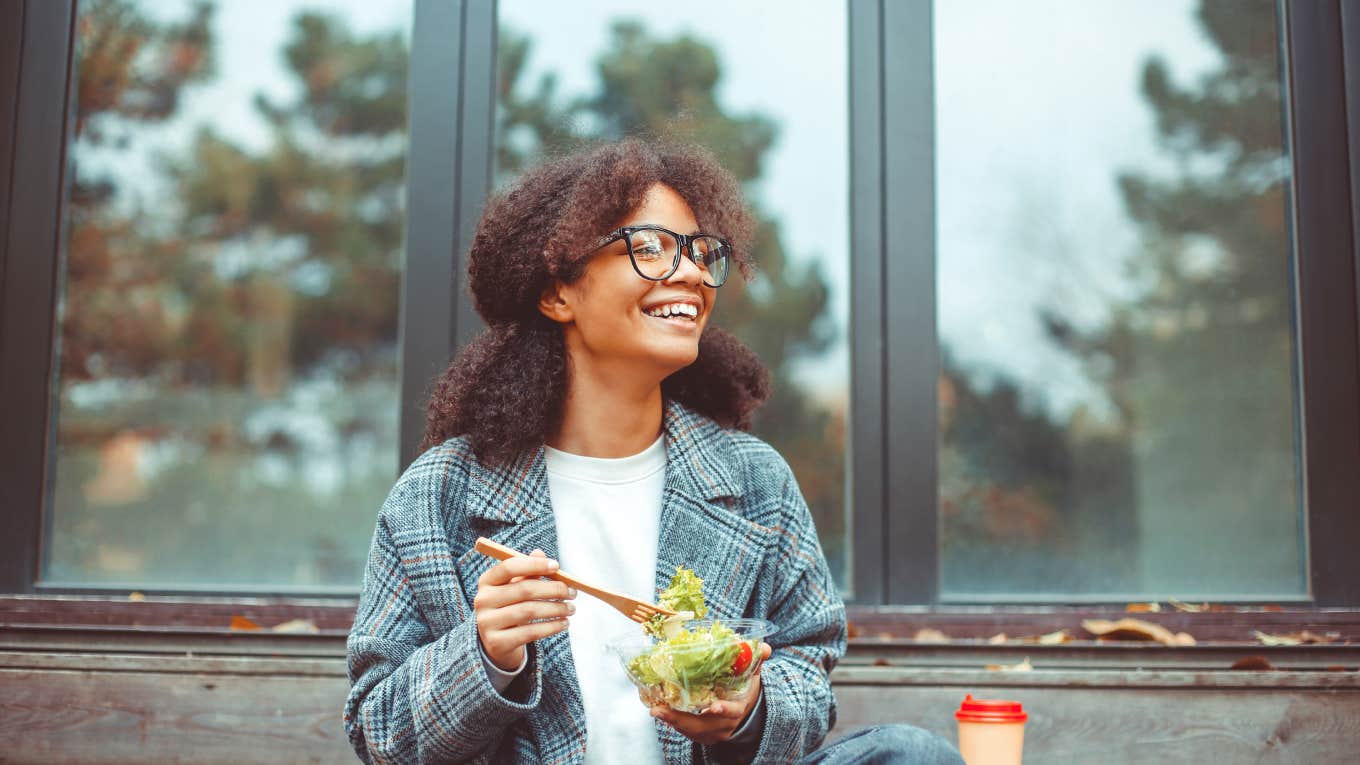 Worker Asks If She's Greedy For Eating 5 Of The 10 Desserts Someone Brought In For Everyone To Share office worker eating salad and smiling at camera while sitting on bench in park outdoors