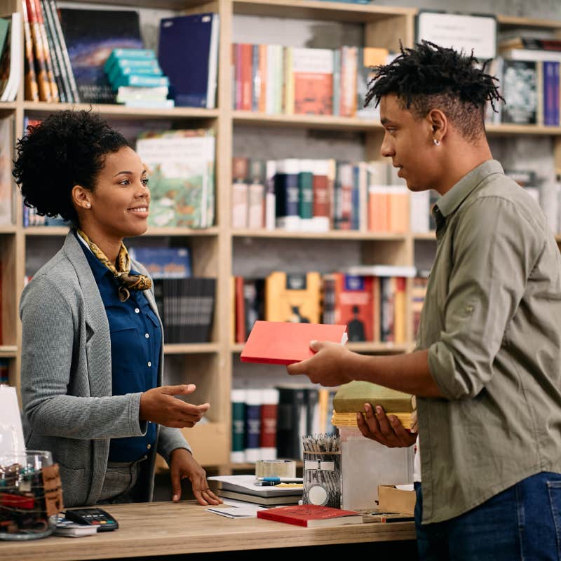student talking to librarian while returning book at the library.