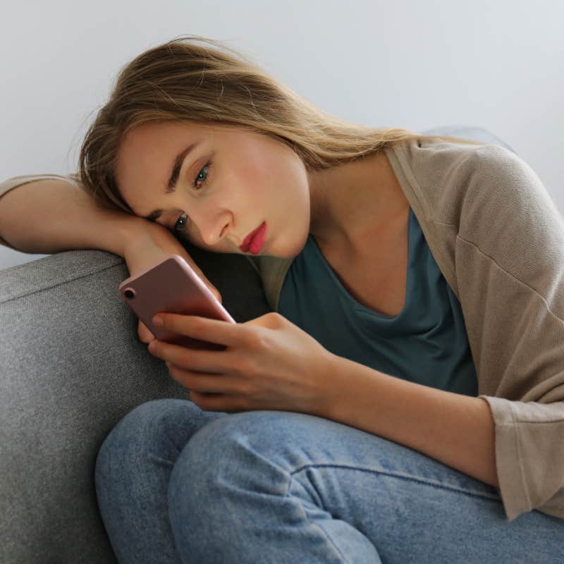 upset woman sitting on couch staring at phone