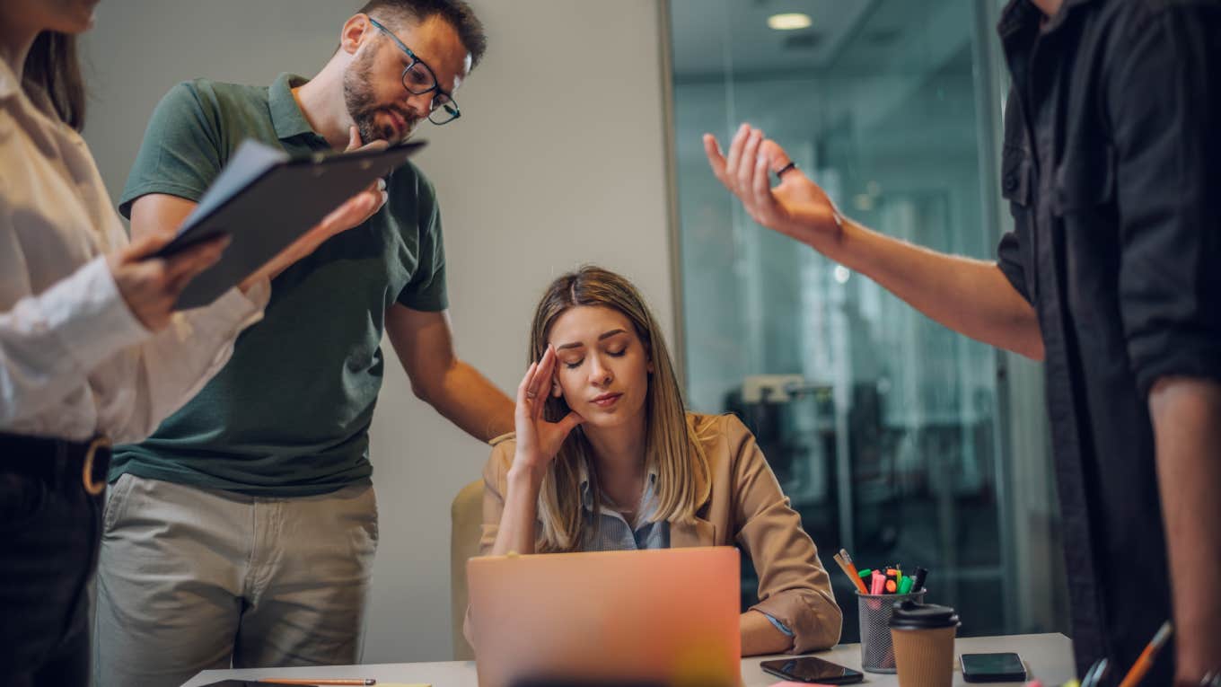 Woman Shaken Up After Her Former Boss Showed Up Unannounced At Her New Job stressed employee sitting at desk in front of laptop with colleagues