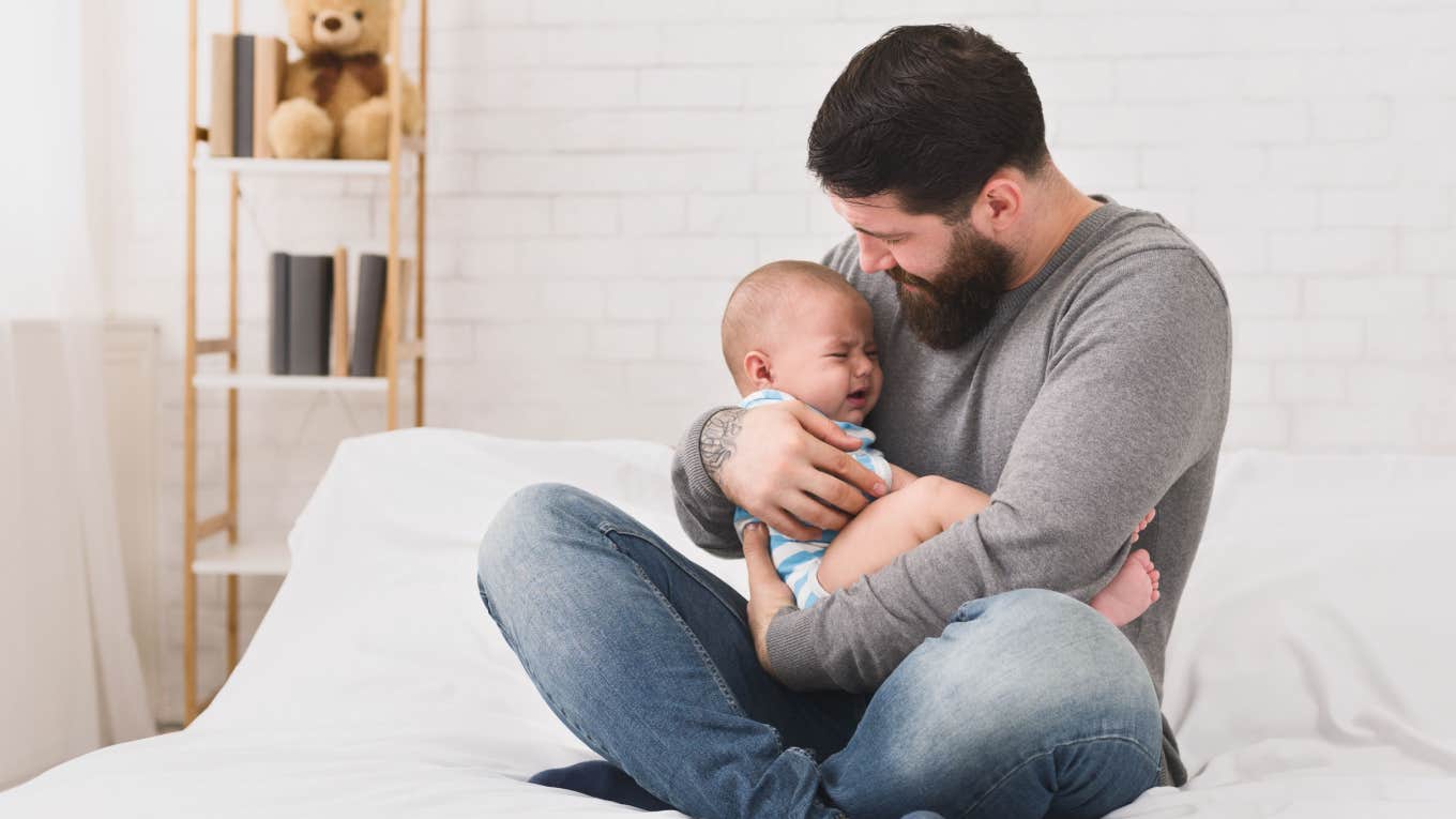 Dad Says He Feels 'Useless' As A Father To His 1-Year-Old Son dad trying to calm crying baby down on bed at home